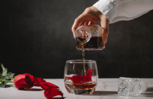 Butelki na nalewkę – warto wyposażyć się w wyjątkowy produkt dłoń_nalewająca_alkohol_z_karafki_do_szklanki_i_róża_obok